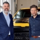 a photo op picture of two men standing in front of a yellow truck